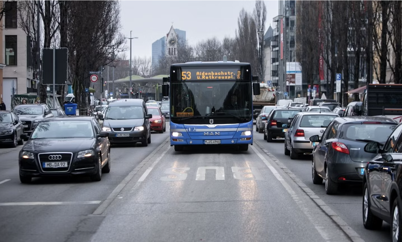 Stadtstraße mit blauem Linienbus in der Mitte, umgeben von vielen Autos, dichter Verkehr